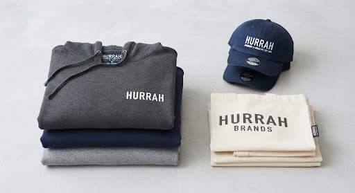 Folded hoodies, a cap and a tote bag printed with the brand name
